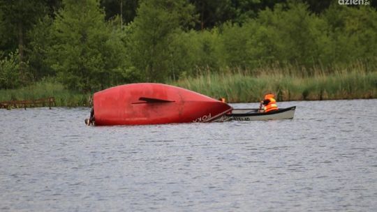 Przewrócona żaglówka. Dorośli i dziecko w wodzie