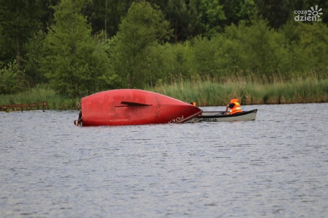 Przewrócona żaglówka. Dorośli i dziecko w wodzie