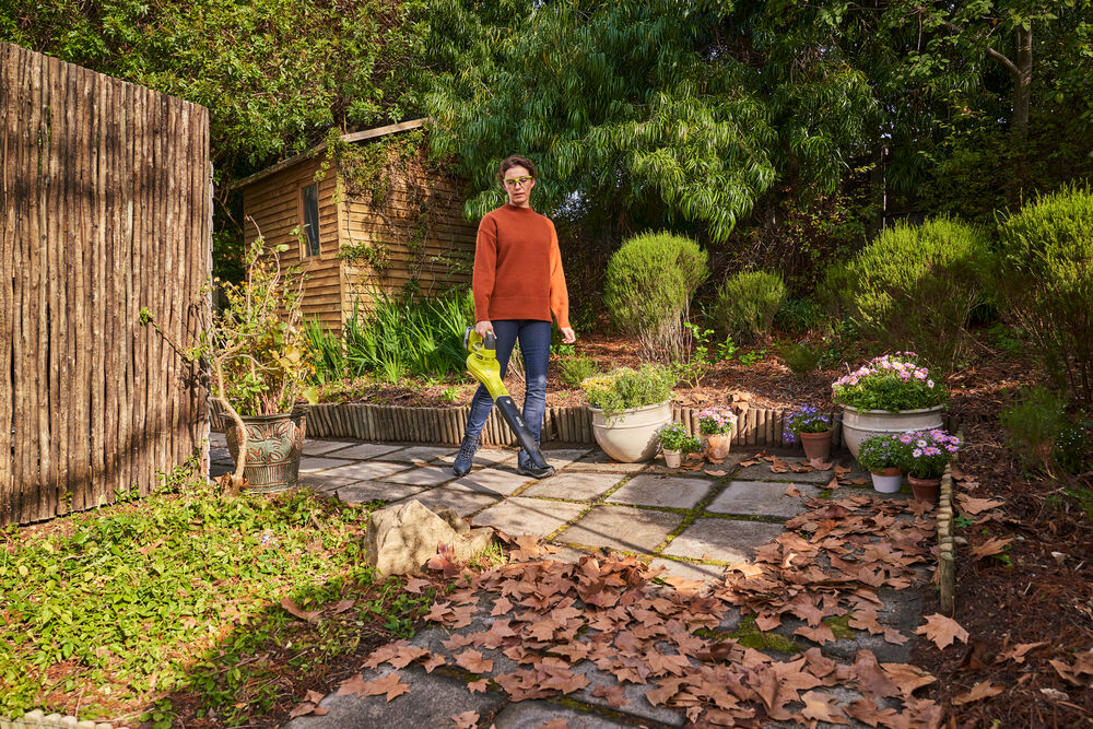 Kobieta w jesiennym ogrodzie sprząta liście z użyciem dmuchawy na akumulator RYOBI