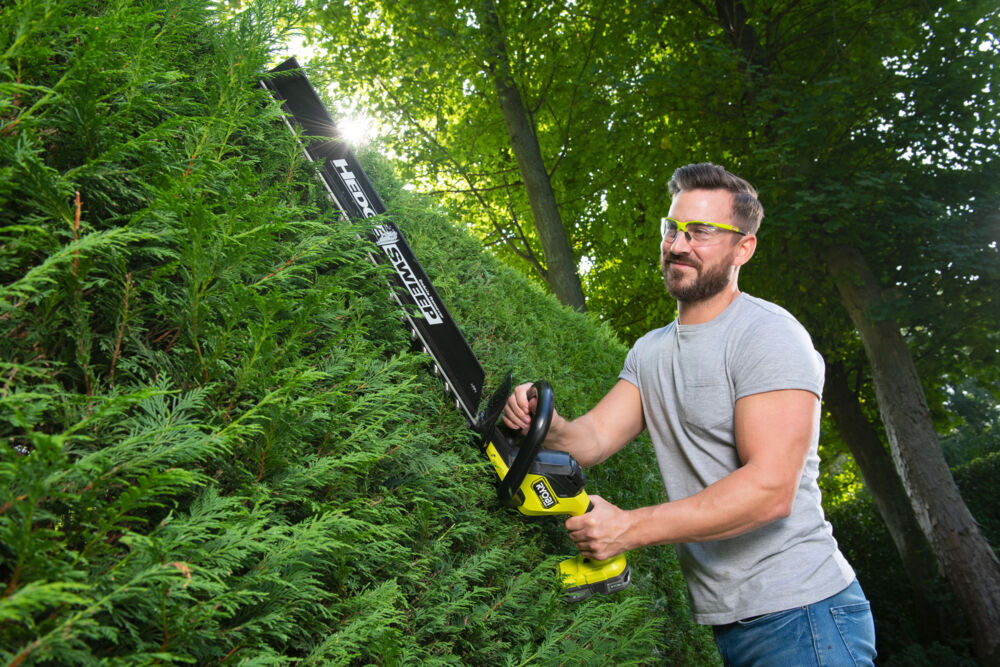 Mężczyzna przycina żywopłot z pomocą nożyc akumulatorowych RYOBI